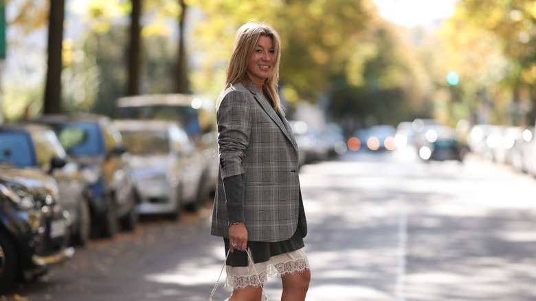 A woman walks down the street wearing a blazer that covers a dress with a lace trim on the skirt
