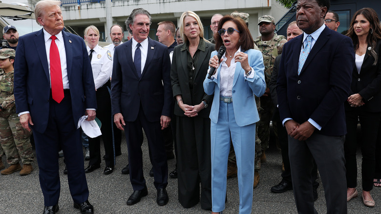 Pam Bondi wearing a baggy green suit next to Jeanine Pirro and Donald Trump
