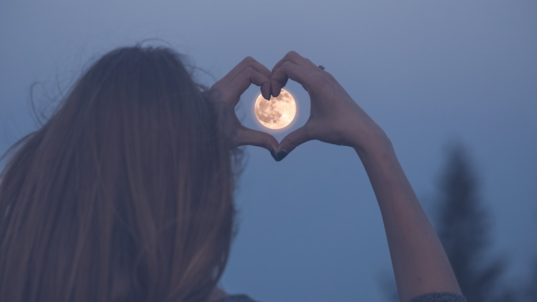 Woman making heart symbol over full moon