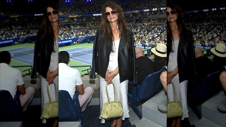 Katie Holmes wearing a dress, green bag, and black leather jacket at the US Open.