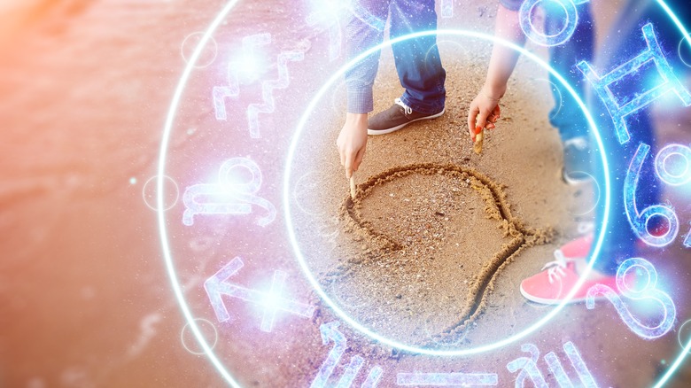 Couple drawing heart in sand 