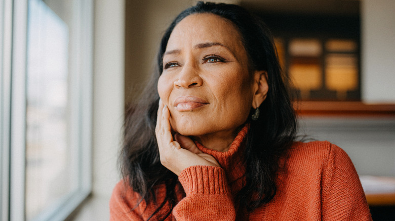 A woman with a few facial wrinkles gazes out a window