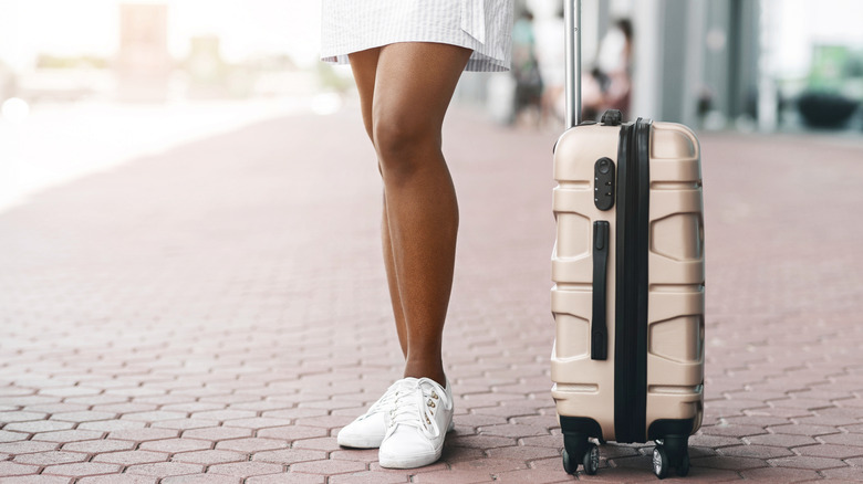 A person's legs standing next to a suitcase, wearing white sneakers