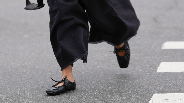 A woman wearing black pants and black square-toe ballet flats