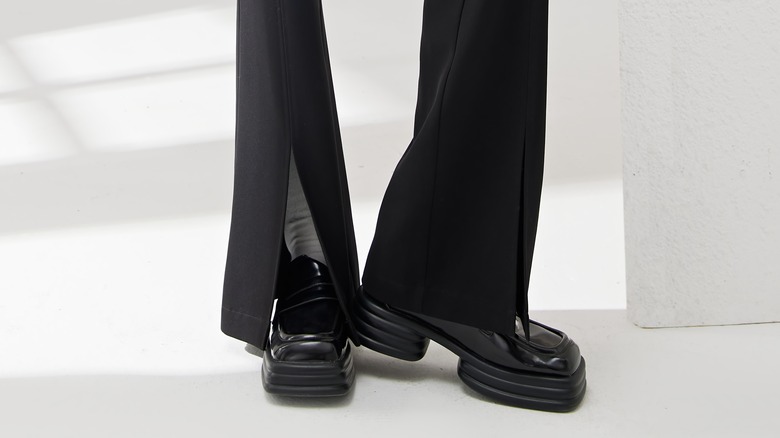 A person wearing black pants with slits and black loafers
