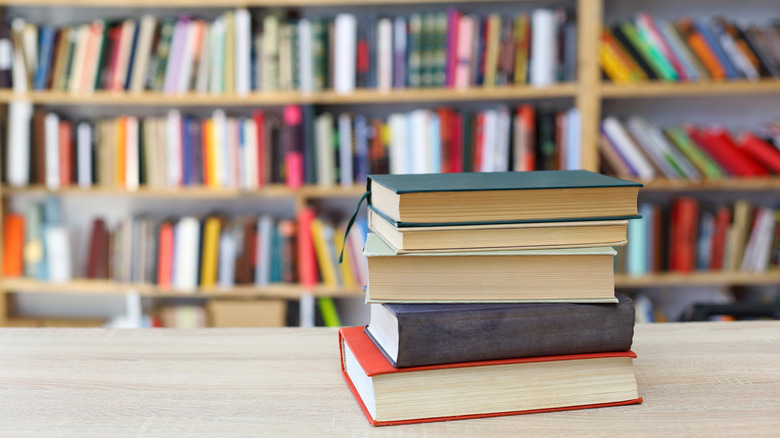 A stack of books on a table in front of a wall full of books
