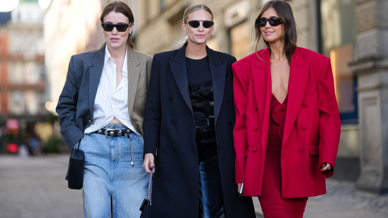 Three women walking - one in red, one in black and navy, and one in gray-and-brown pinstripes