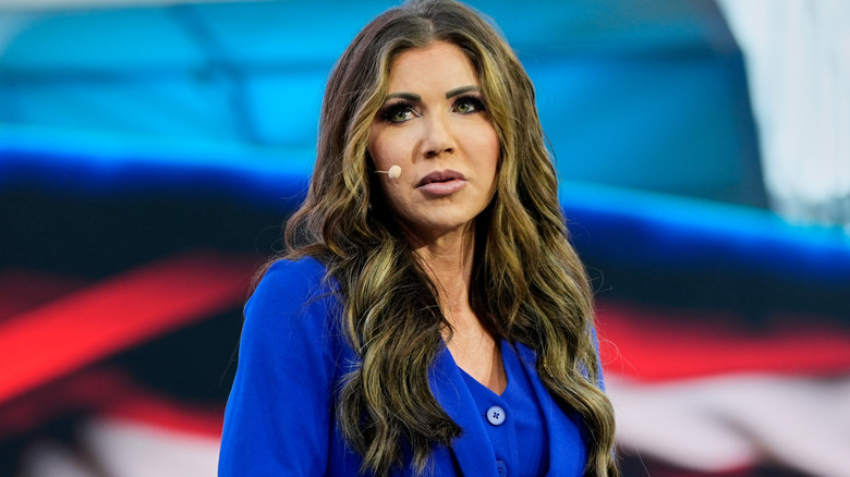 Kristi Noem wearing a blue jacket with a full face of heavy makeup