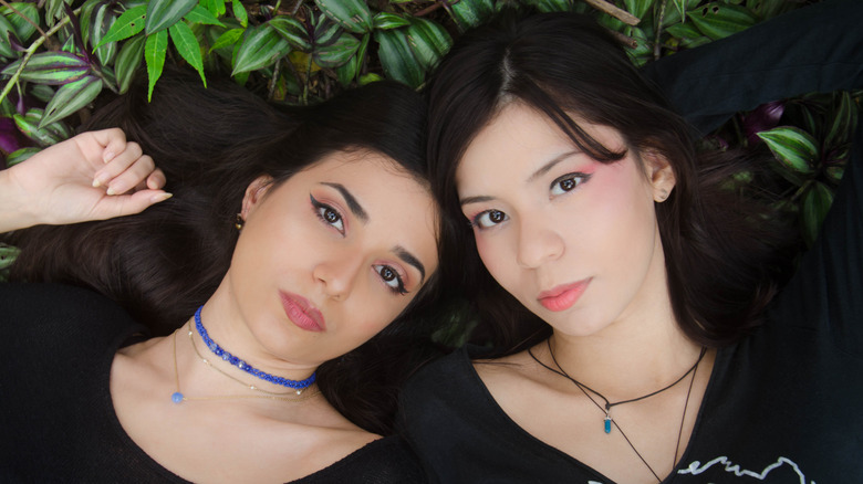 Two women lying on foliage together and one wearing a choker
