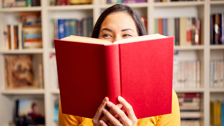 A smiling woman holding a book in front of her face.