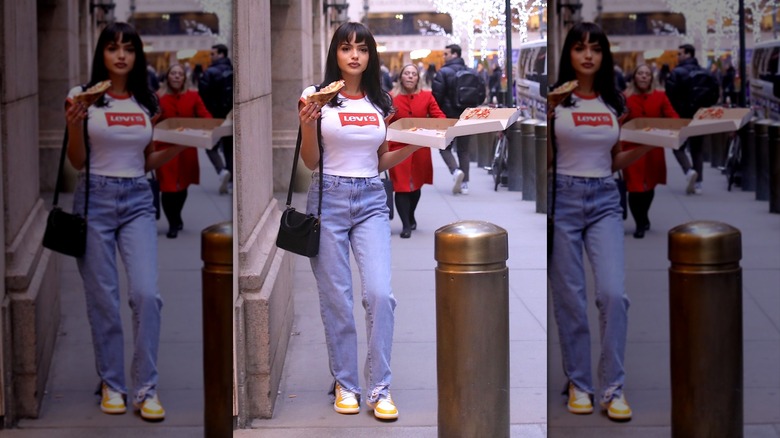 A woman eating pizza in jeans and a white Levi's tee and yellow sneakers