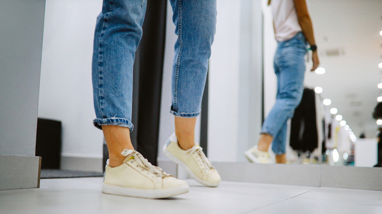 Person looking at their yellow sneakers in the mirror while wearing jeans and a tee