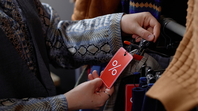 A woman checking the price tag on clothes at a thrift store