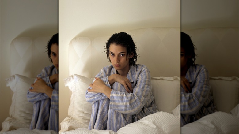 Winona Ryder posing on her bed in blue striped pajamas and wet hair.