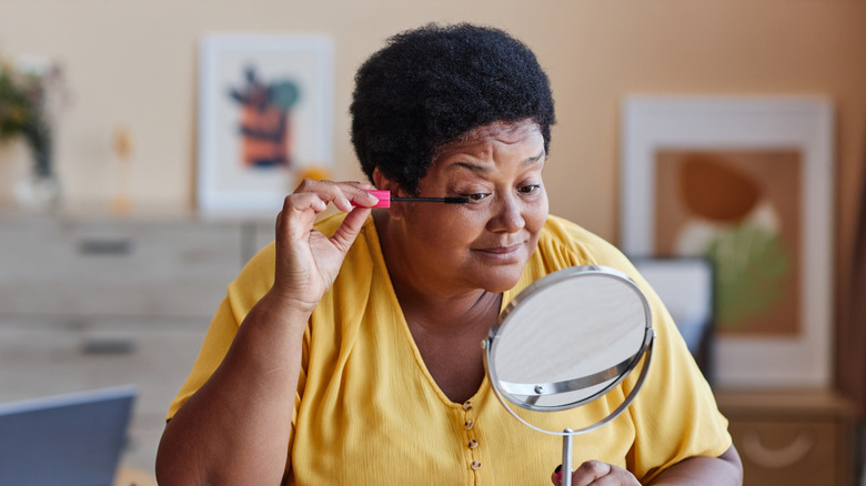 Woman in a yellow shirt applying mascara