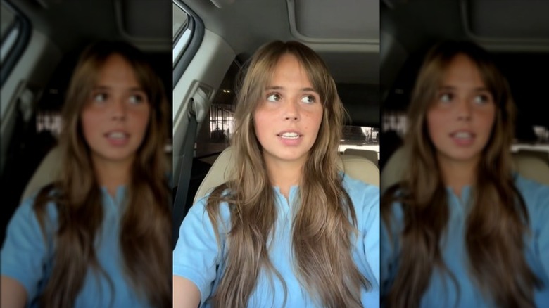Girl seated in car with bottleneck bangs