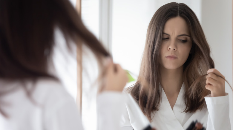 Woman holding her destroyed hair looking in mirror