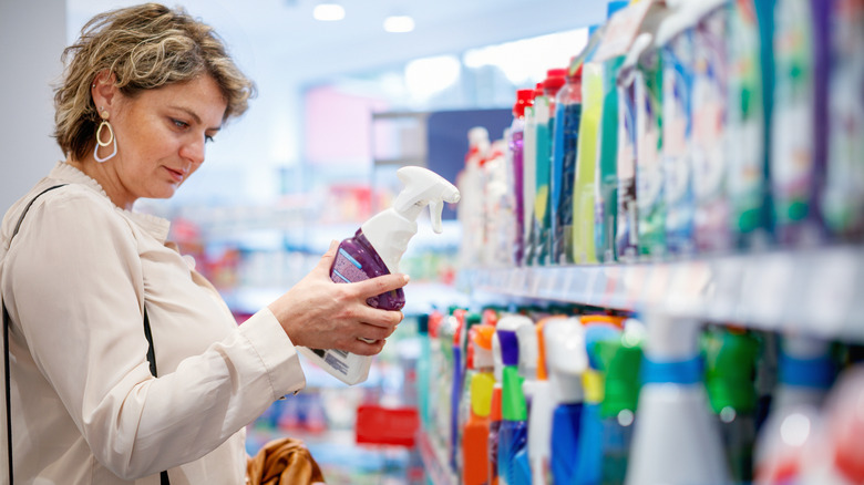 A woman inspecting a cleaning product in a supermarket to decide which to purchase
