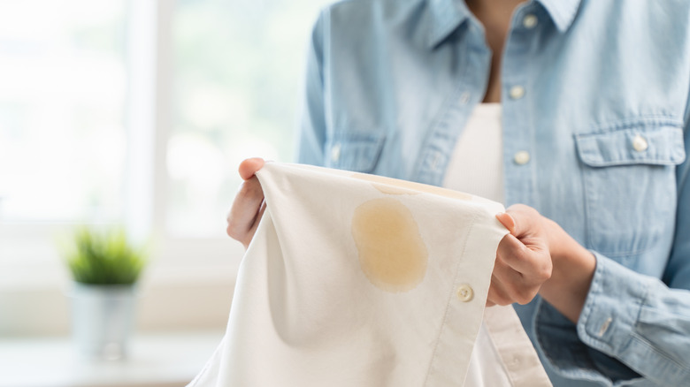 A person holding a white shirt with a set-in brown stain