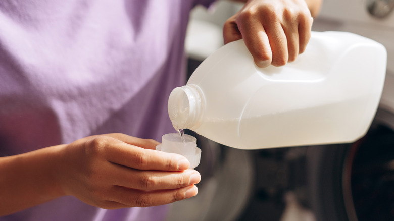 A person wearing a purple shirt pouring liquid detergent into the measuring cap to spot treat