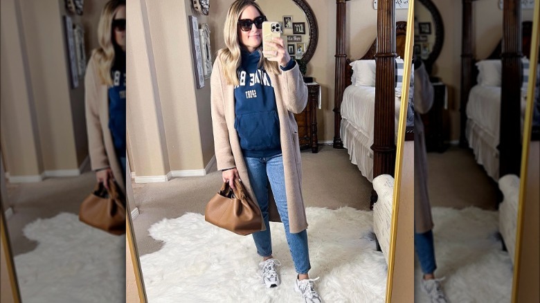 Woman takes selfie wearing tan coatigan, jeans, and hoodie