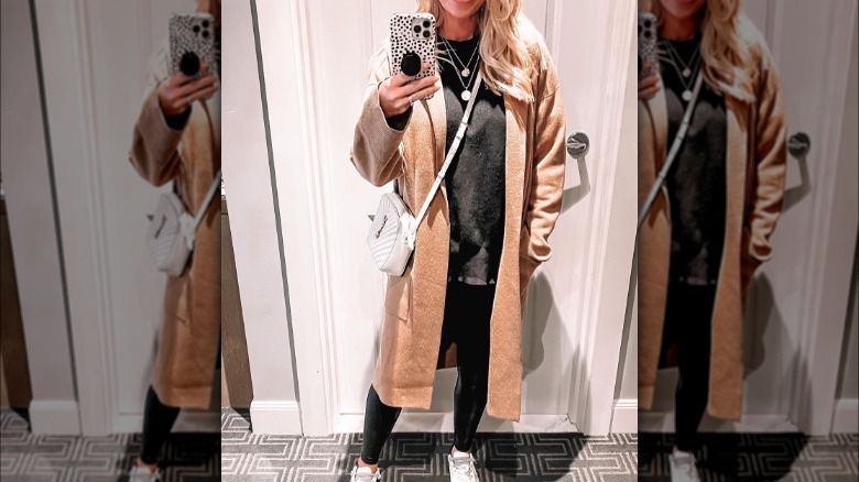 Woman takes selfie in black tee and legging with camel coatigan