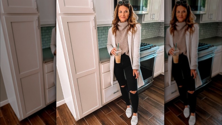 Woman poses in kitchen wearing sweater, coatigan, and ripped skinny jeans