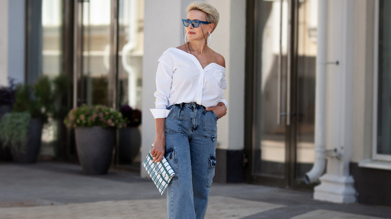 An older woman wearing a white blouse, slides, and jeans.