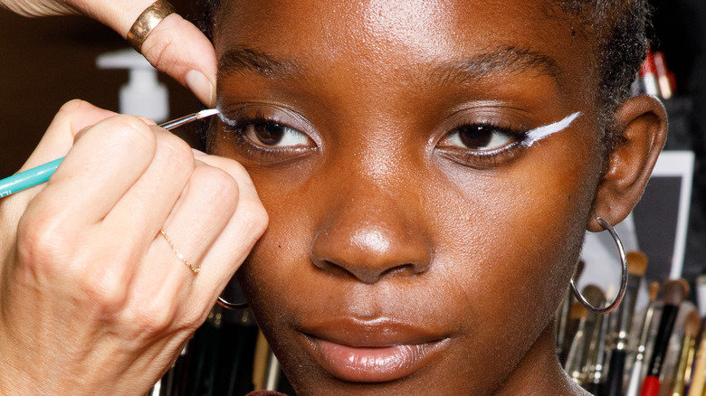 applying white liner on woman's eyes