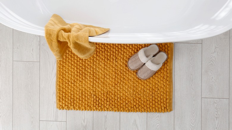 yellow bathmat in front of bathtub