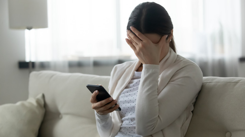 Woman distressed with hand over face reacting to phone in hand