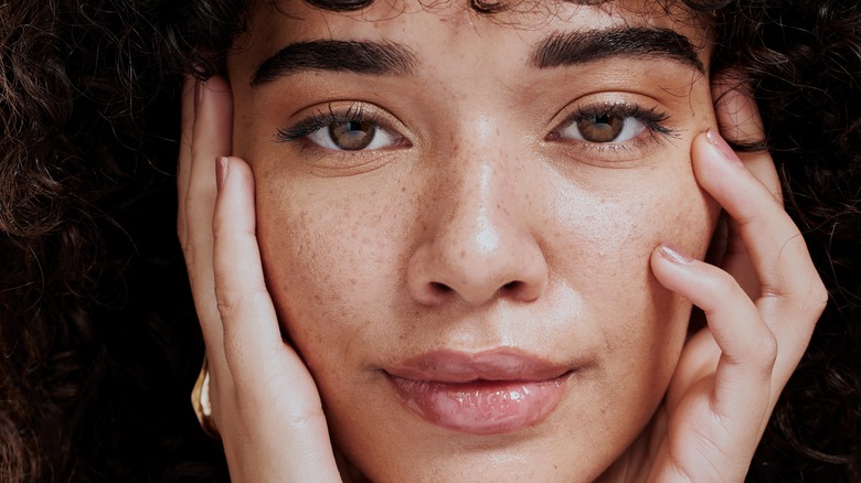 young woman with flawless skin touching face