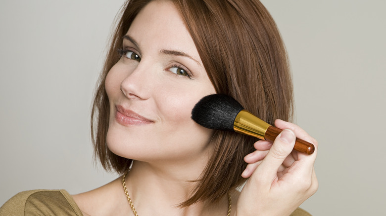 Smiling woman with red hair applying makeup