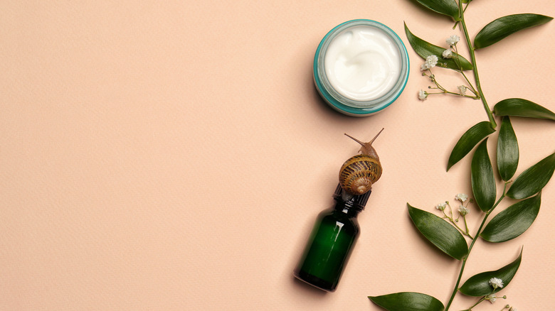 a snail crawling on top of a bottle next to cream 