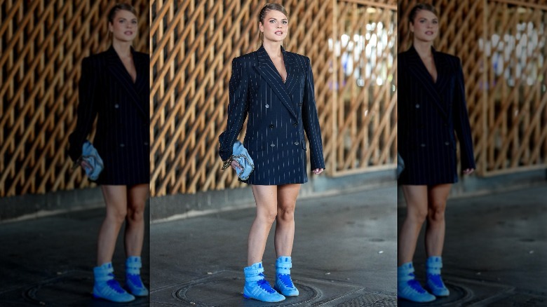 A woman wearing a black blazer dress with bright-blue sneakers