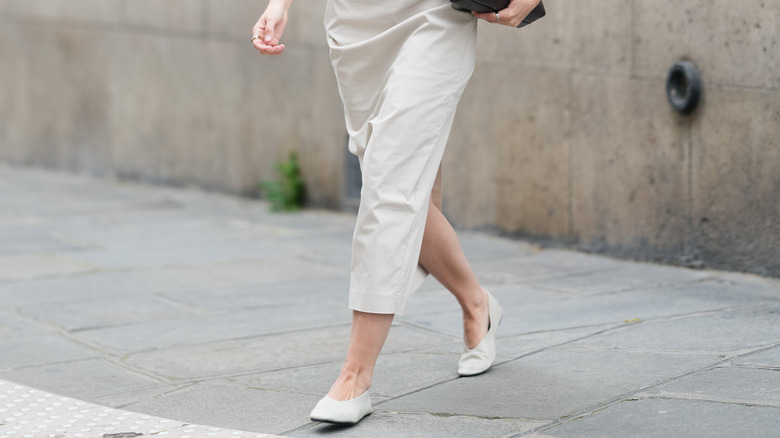 Closeup of a woman's feet wearing white almond-toe ballet flats.