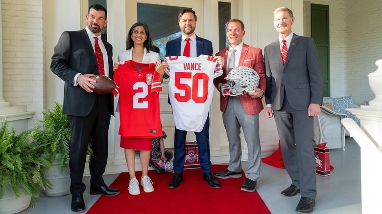 Usha Vance, wearing a red dress, white blazer, and white sneakers, poses with JD Vance and guests at a reception for the Ohio State University.
