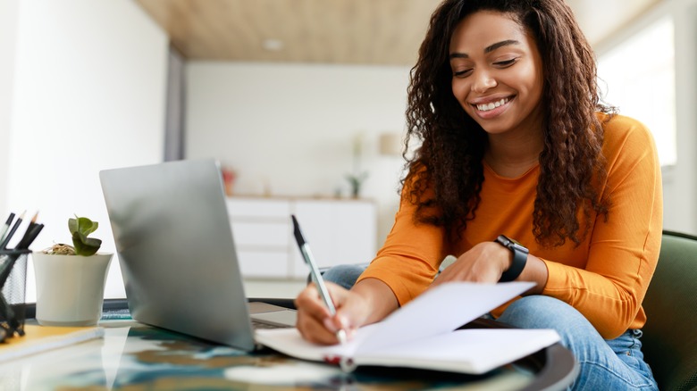 person writing in notebook and laptop