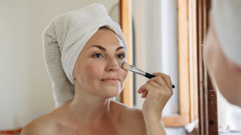 A woman uses a brush to apply liquid foundation makeup to her face