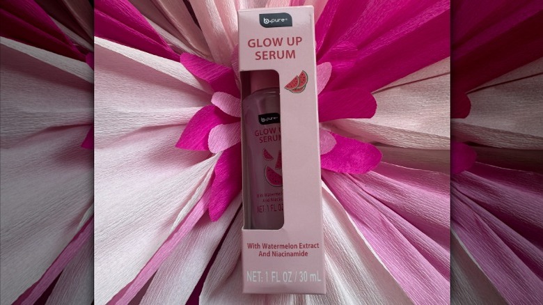 A bottle of B.Pure's Glow Up Serum on a floral backdrop