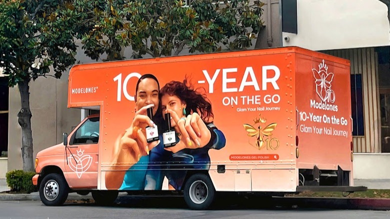 An orange Modelones truck is fully blinged out with the nail brand's logo and marketing