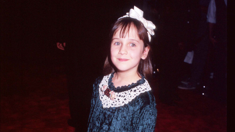 Mara Wilson as a child wearing a navy blue velvet dress with a white bow in her hair