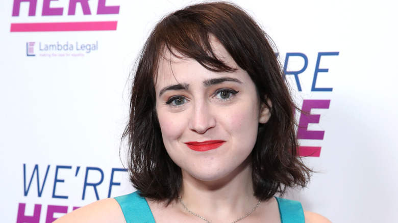 Mara Wilson wearing a turquoise dress with a red lip on a red carpet.