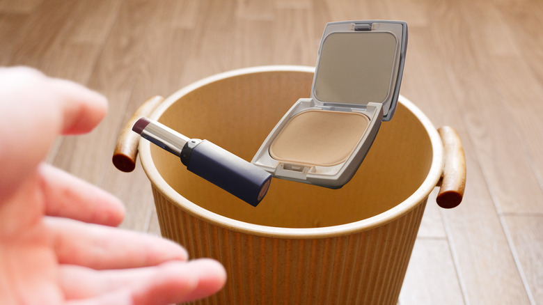 Person tossing foundation and lipstick into trash