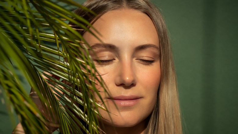 Woman wearing minimal makeup standing behind leaves