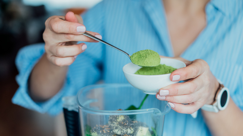 woman adding green powder to smoothie