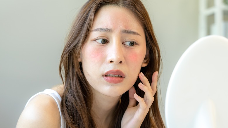 Model looking at red skin in mirror
