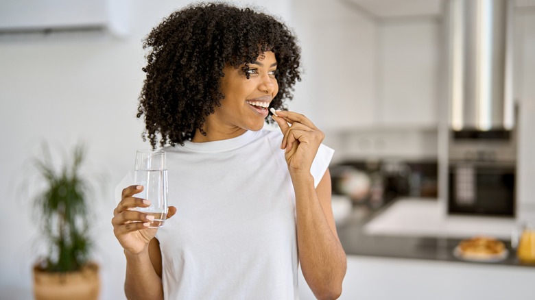 A woman taking a supplement with a glass of water