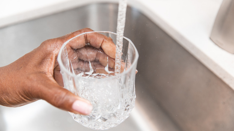 A woman filling a glass with water from a tap