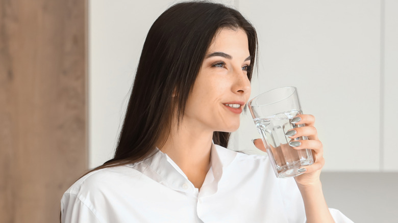 A woman lifting a glass of water to her lips to take a drink